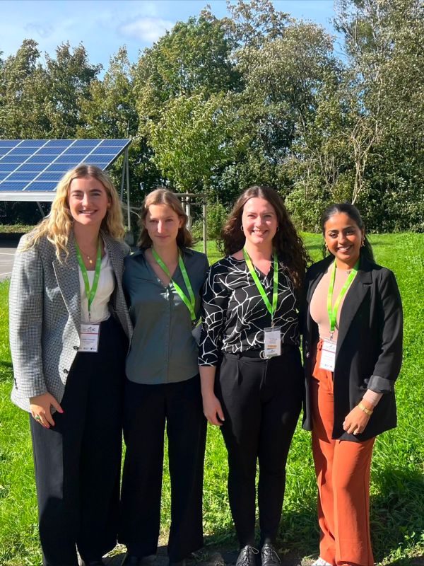 Four students together in a field surrounded by trees and solar panels 