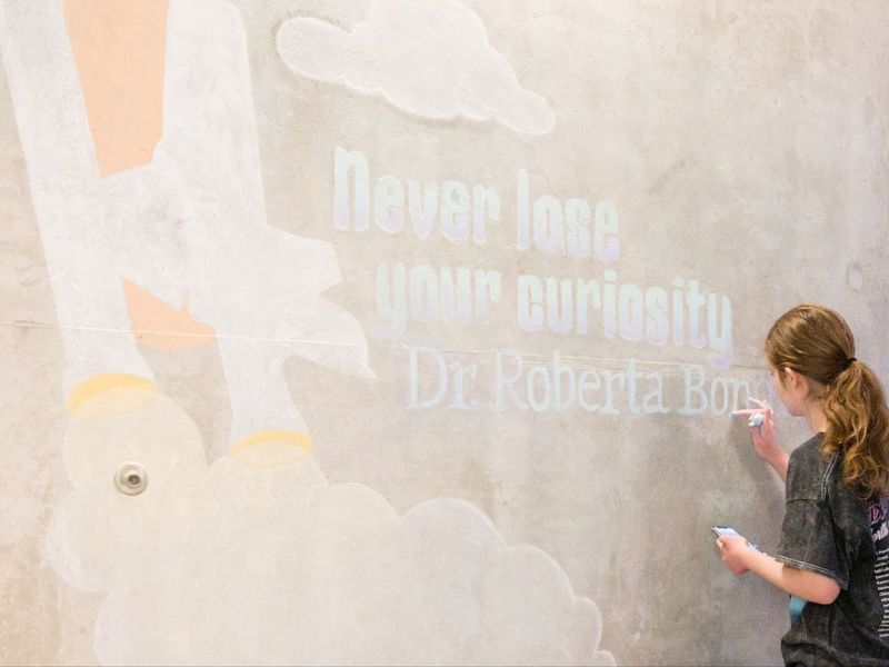A student using colorful chalk to draw an inspirational quote on a concrete wall.
