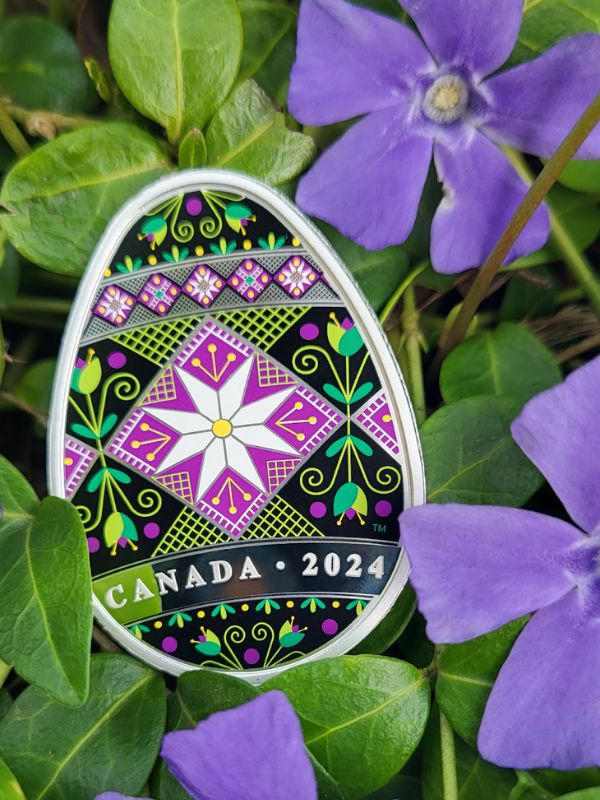 Purple and green egg shaped coin laying on top of purple flower and green plants