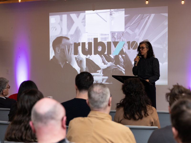 A woman stands in front of a podium addressing an audience 