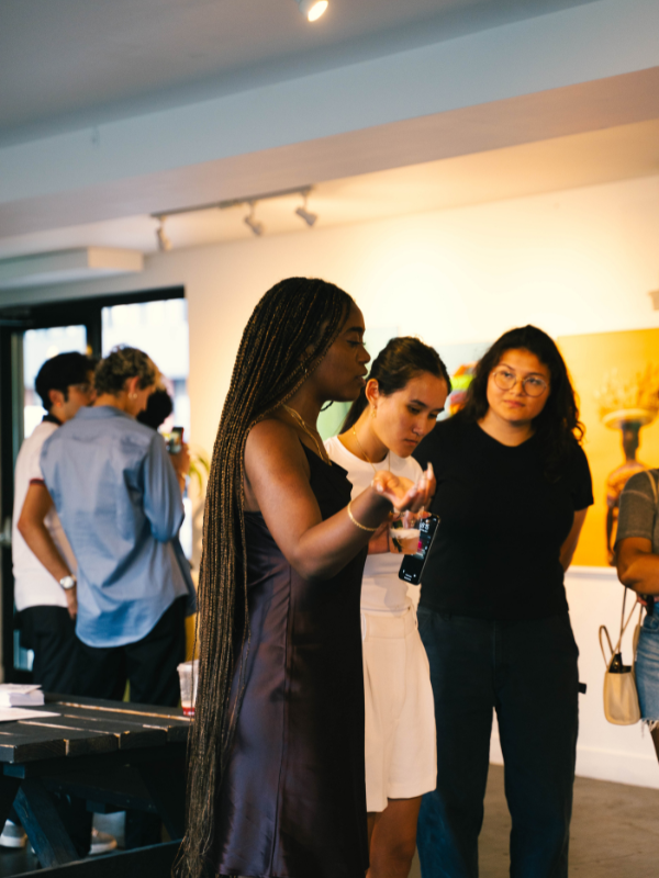 Three poeple are standing in a gallery looking at something off camera.