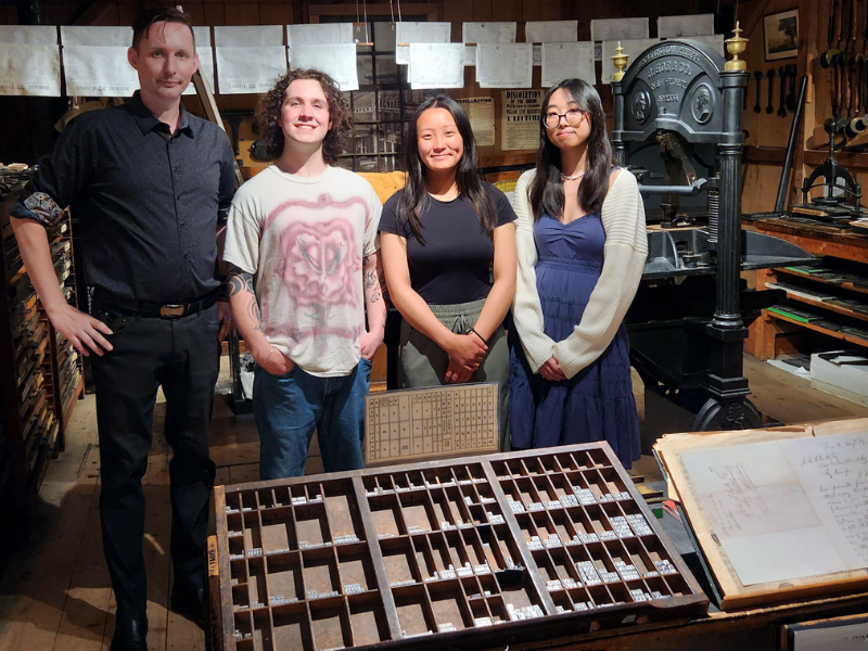 A group shot of four people posing among old printing equipment in Mackenzie House, a historical museum.