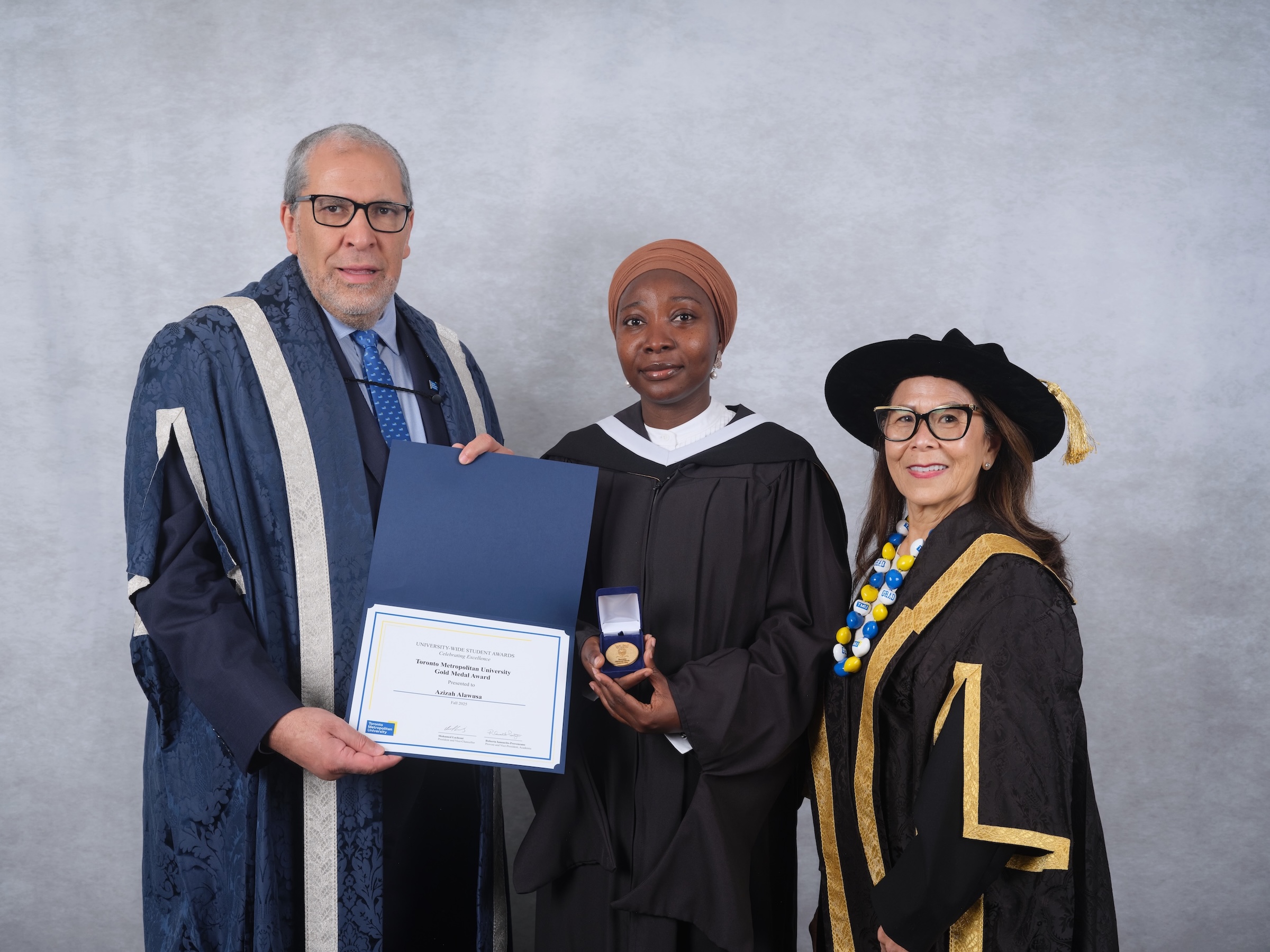 Azizah Adunola Alawusa stands between TMU President Mohamed Lachemi and Chancellor Joanne Chin-Loy Chang, holding her certificate and Gold Medal.
