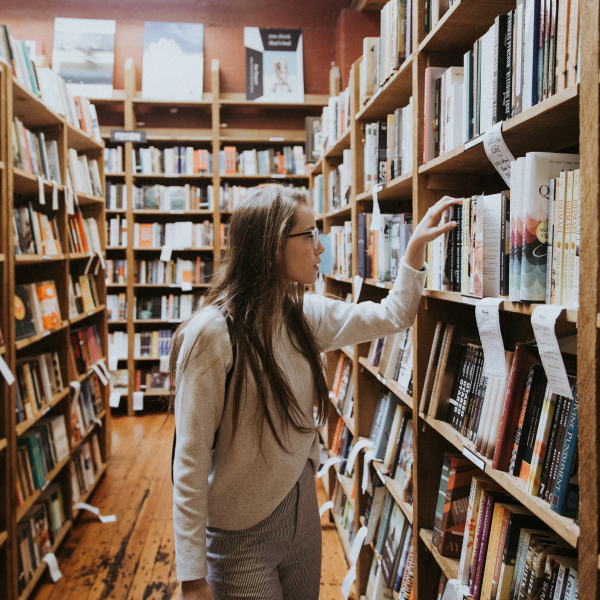 Medium-long shot of a woman in an aisle of a library with a hand reached up to take out a book.