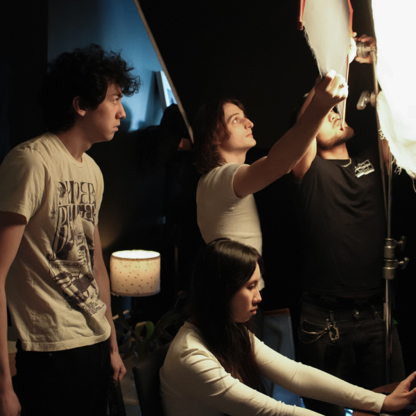 Four people look towards the right as they work together to set up a modifier on a strobe light.