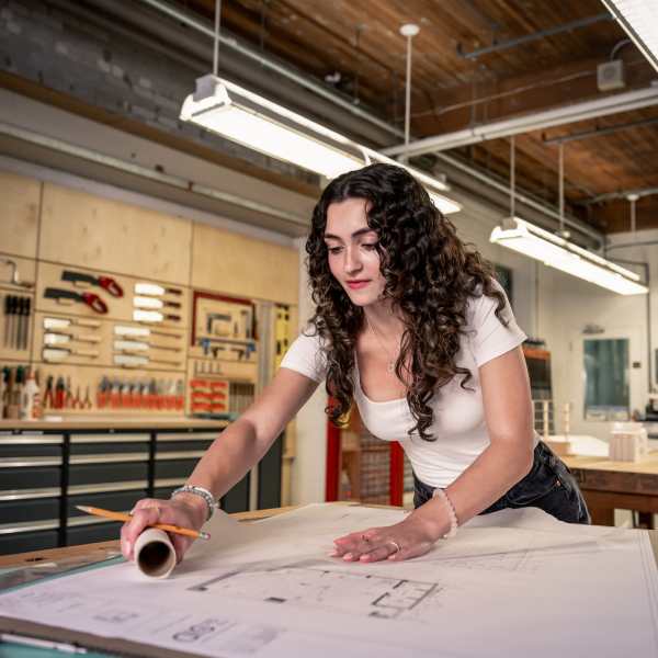 Medium shot of a woman leaning over a table with floor plans on it.