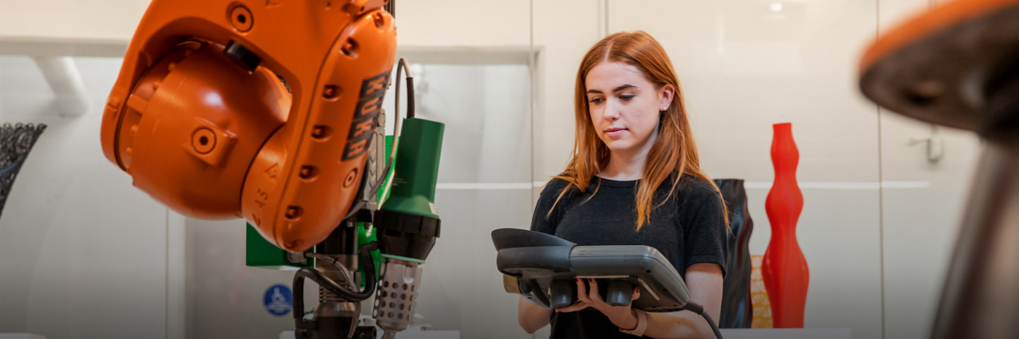 Student working with a robotic (Kuka) arm, with 3d sculptures in the background