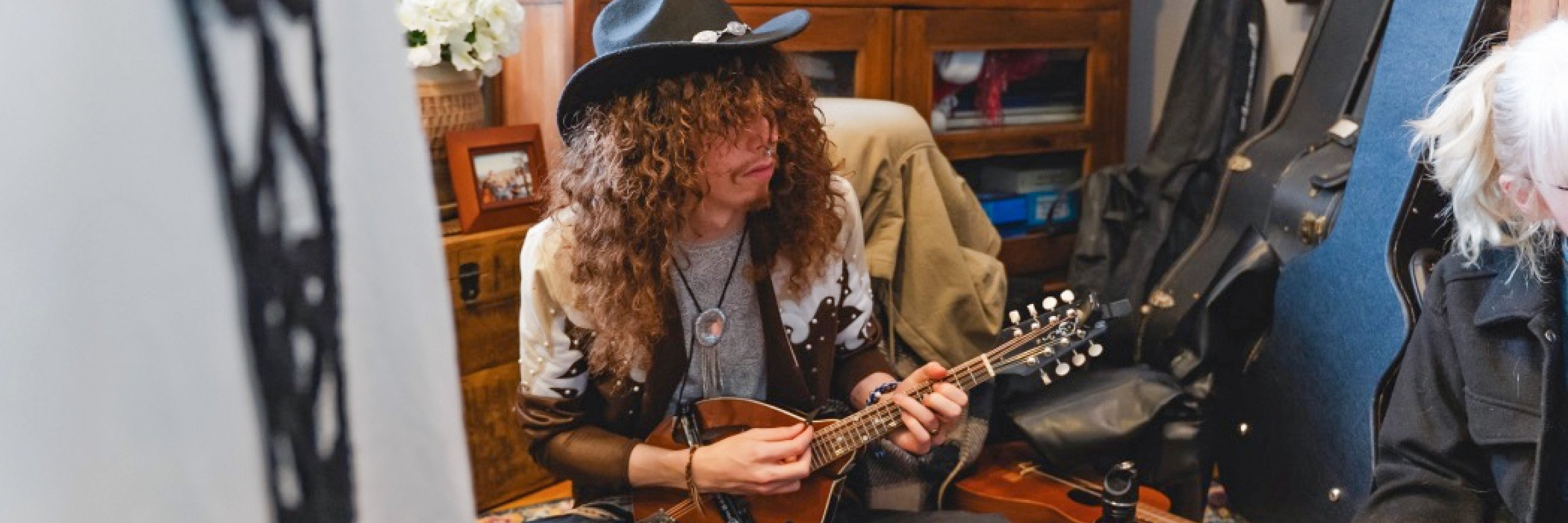Student wearing a black cowboy hat and playing the mandolin