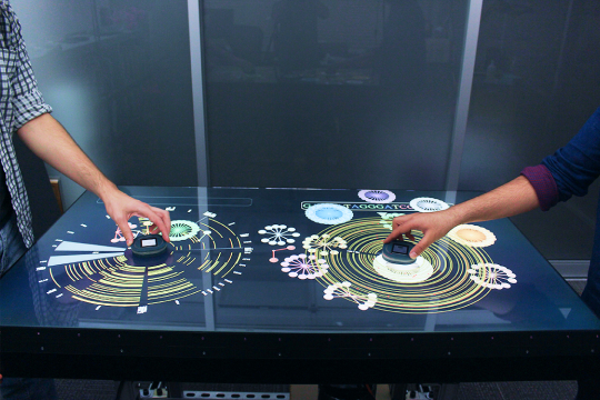 Two arms moving a technology device on a table