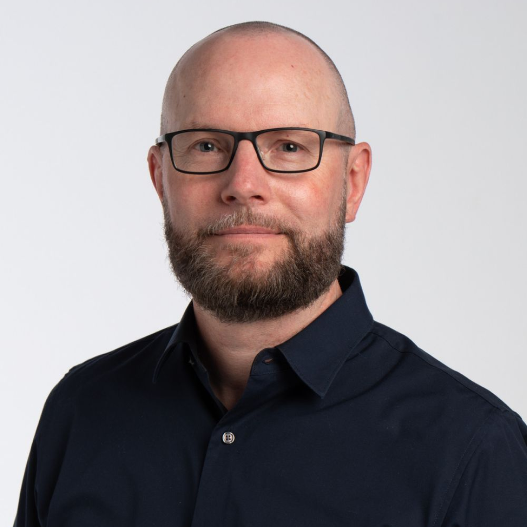 Headshot of James McCrorie wearing black business shirt and smiling