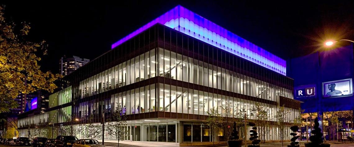 The RIC/IMA building at night with glowing purple lights. 
