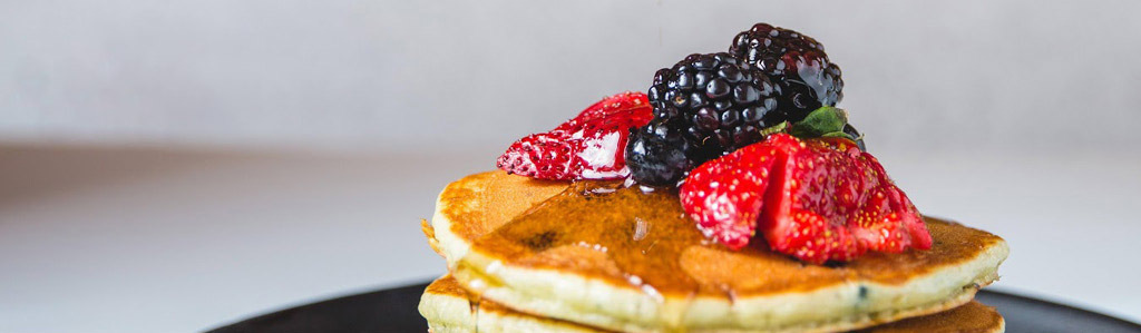 A stack of pancakes with blackberries and strawberries on top.