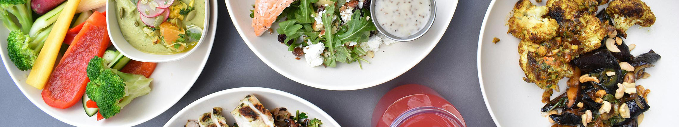 An overhead view of a grey table with four appetizing dishes on white plates.