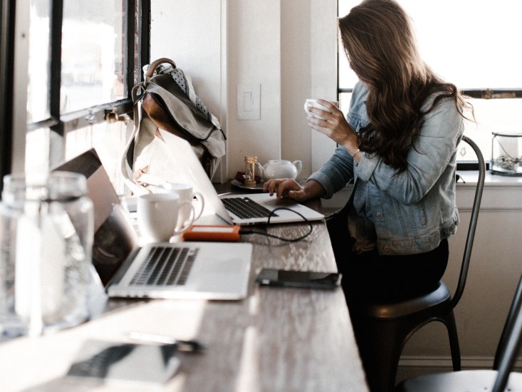 woman holding a coffee cup and working on her laptop