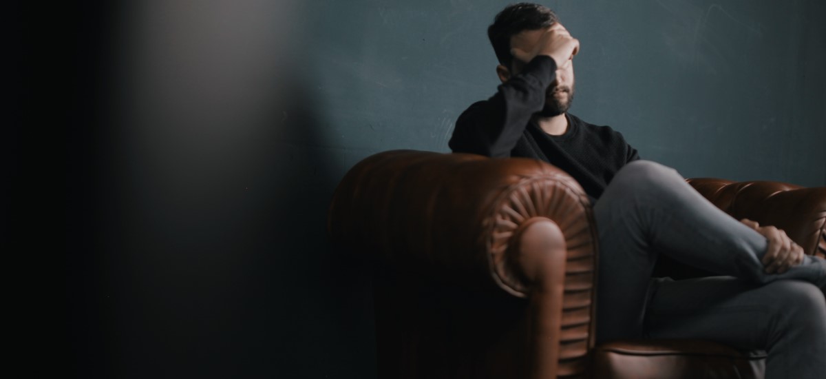 man in the couch with his hand on his forehead