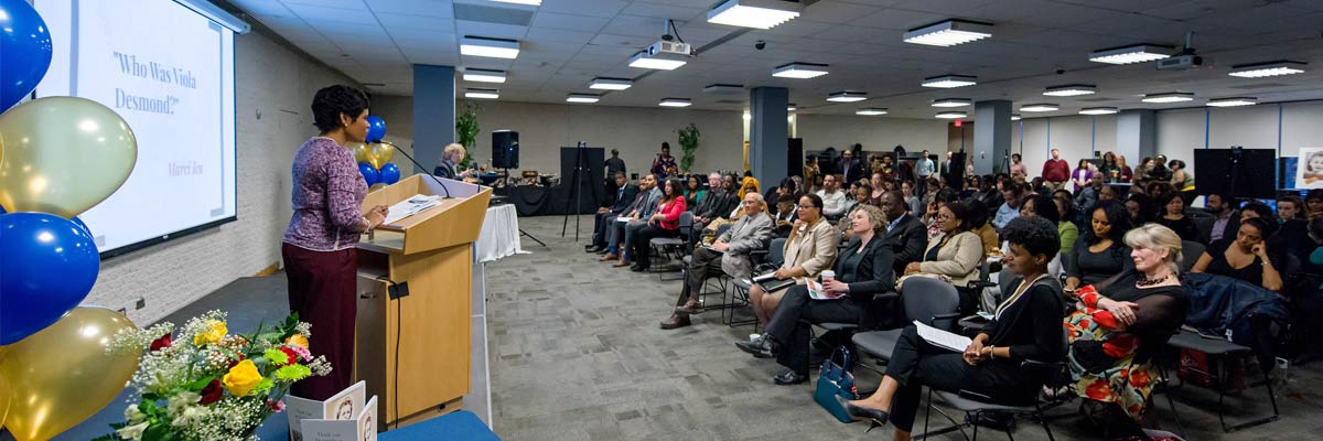 Person speaking in front of a crown in the Commons conference room