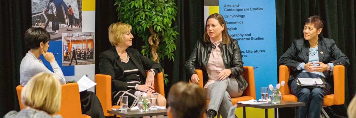 A panel of women speaking to the crowd at a conference or event.