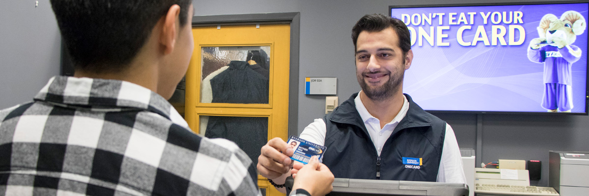 A member of the OneCard team smiling while handing a student their OneCard.