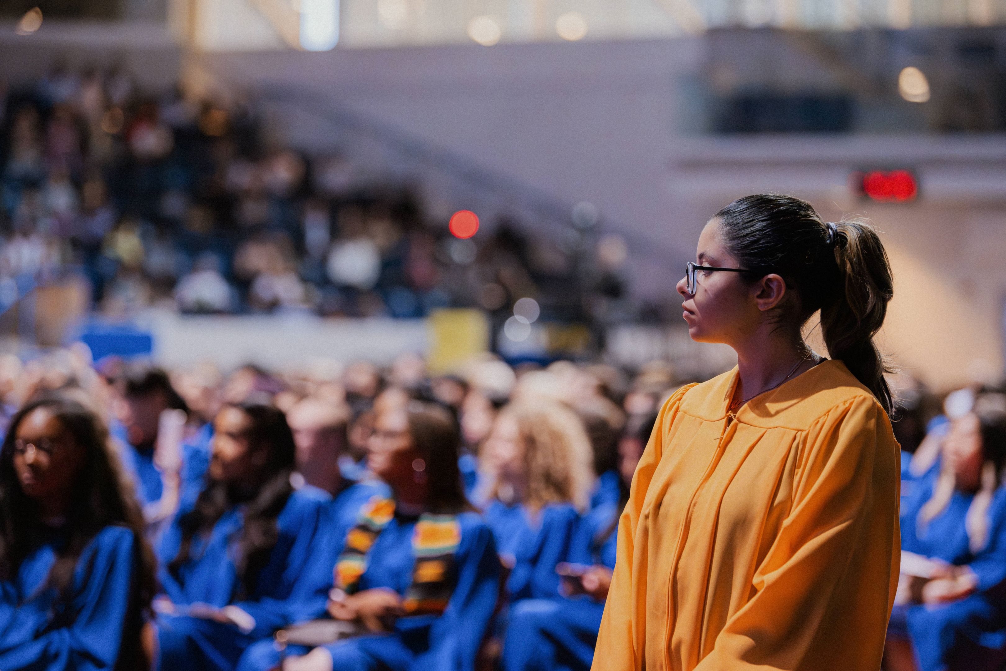 A student staff member in a gold gown standing and watching the ceremony.