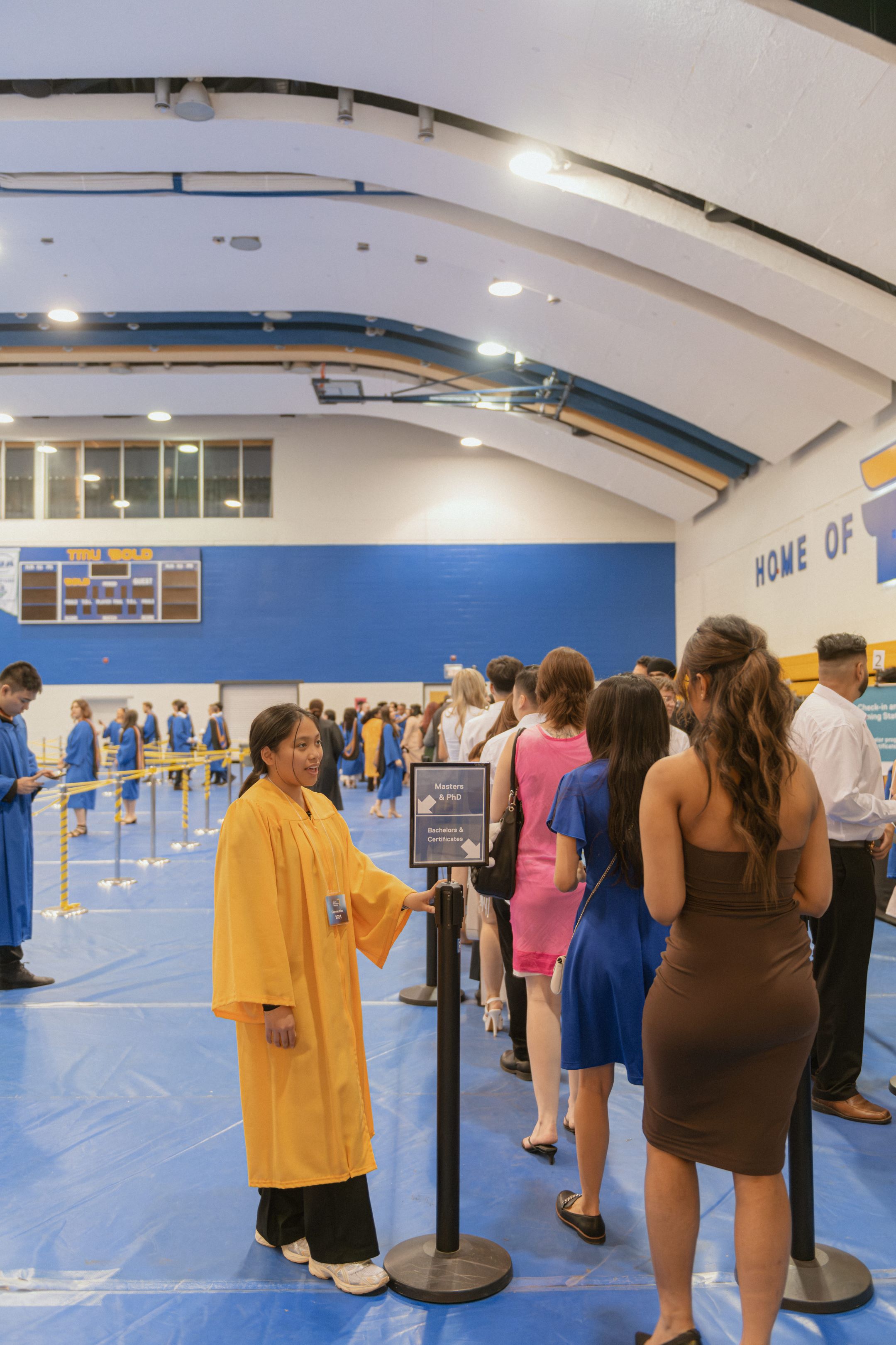 A student staff in a gold gown helping arriving graduates enter a line up.