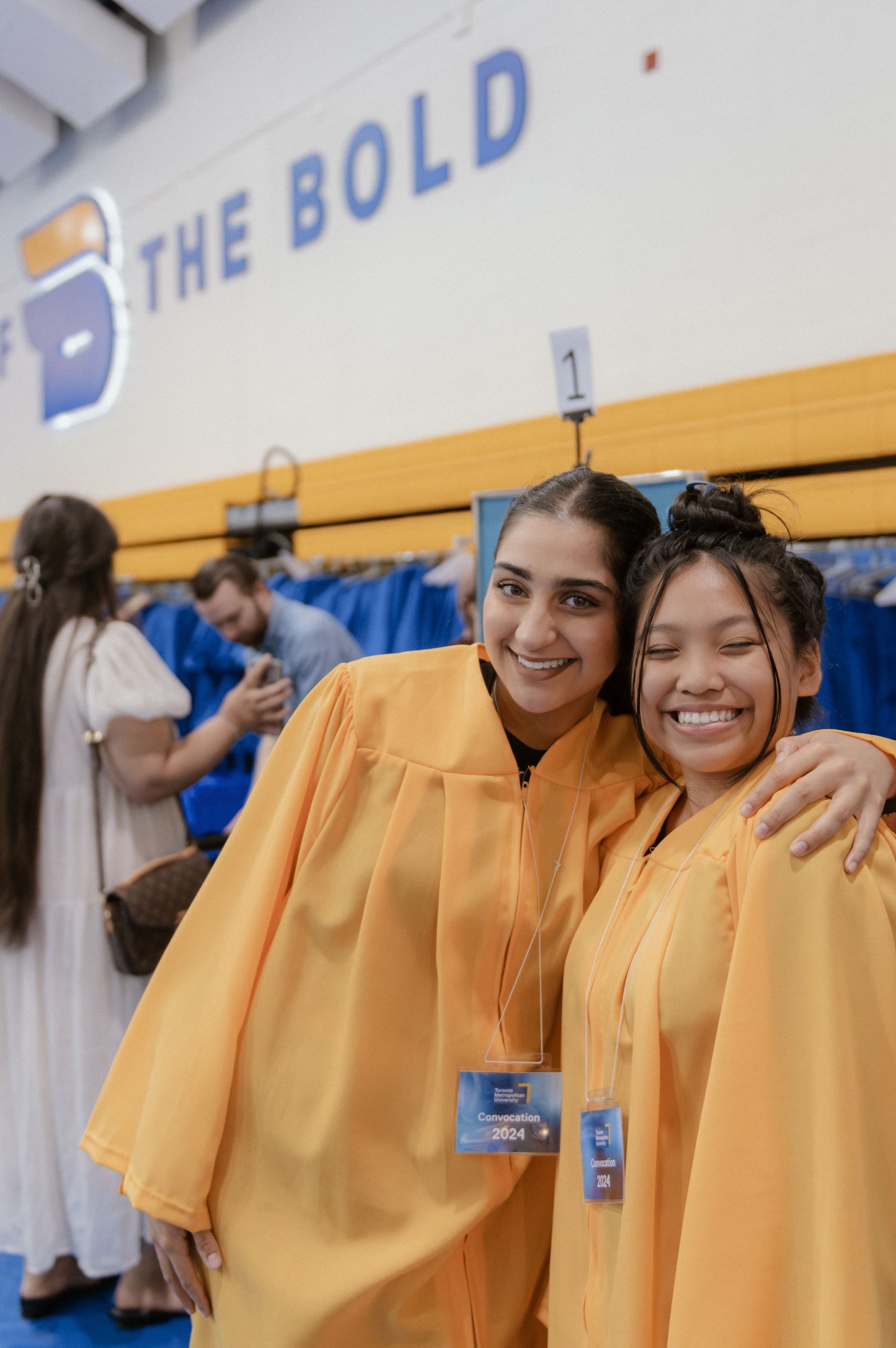 Two people in gold gowns smiling.