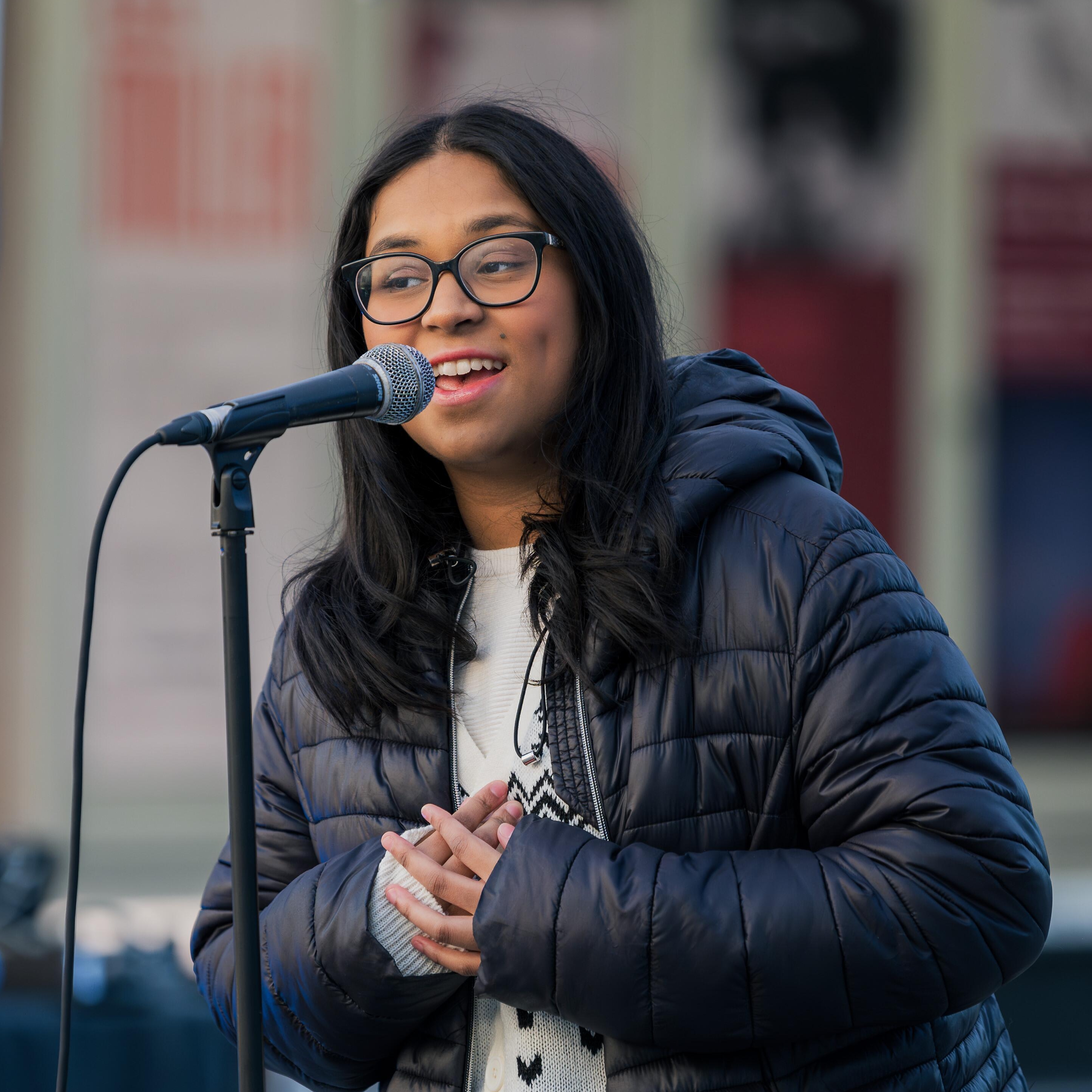 Ramya in front of a microphone, singing.