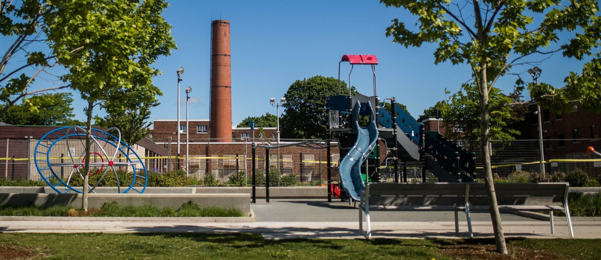 A playground in Regent Park, Toronto, with a smokestack in the background