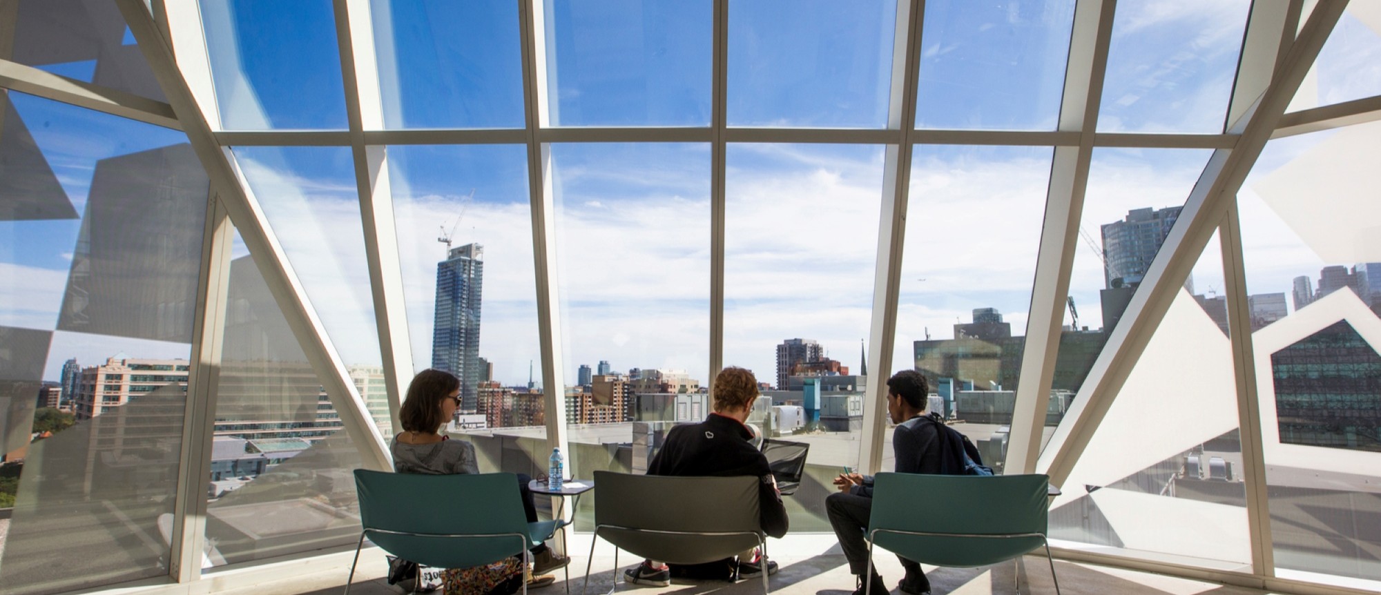 Three seated people in front of large windows overlooking the Toronto skyline