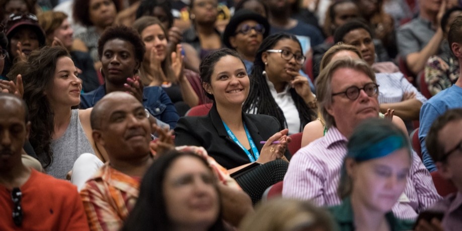 Audience members smiling and applauding during a large event.