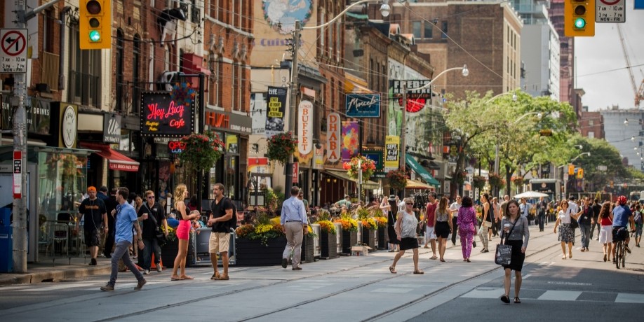 Busy downtown Toronto street filled with pedestrians, storefronts and restaurant patios.