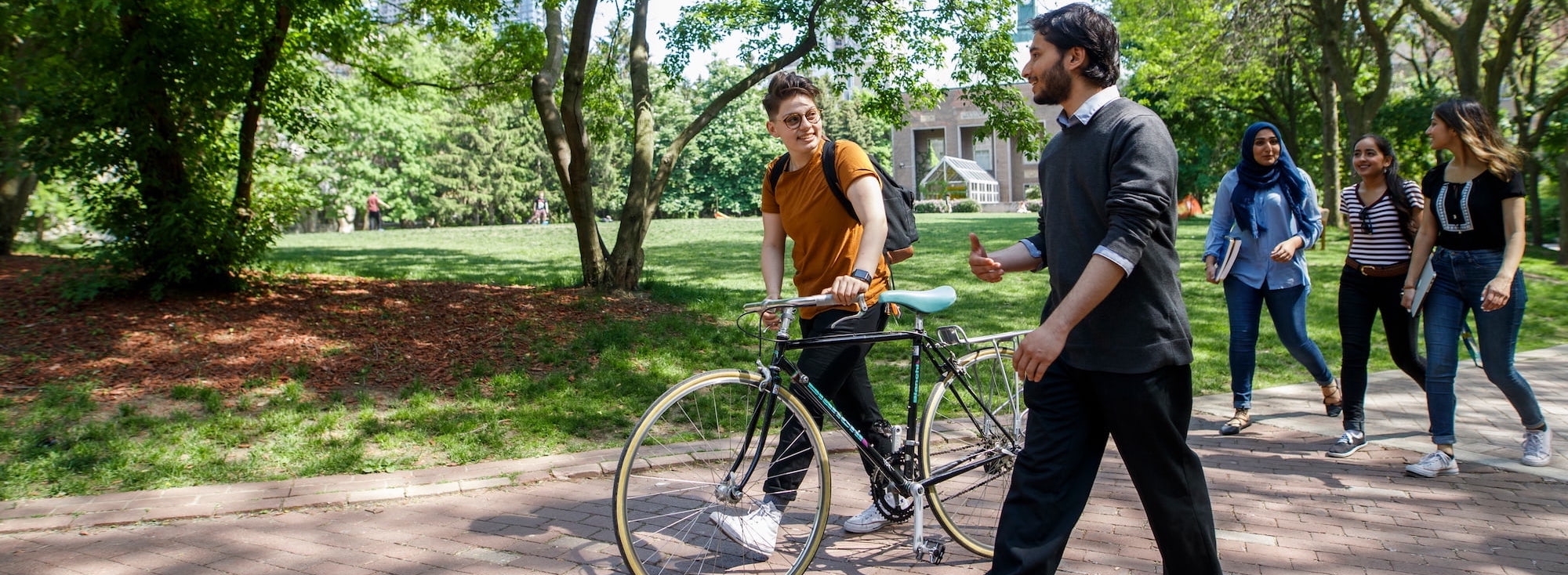 Students walking through the TMU Quad with one student wheeling a bike beside them