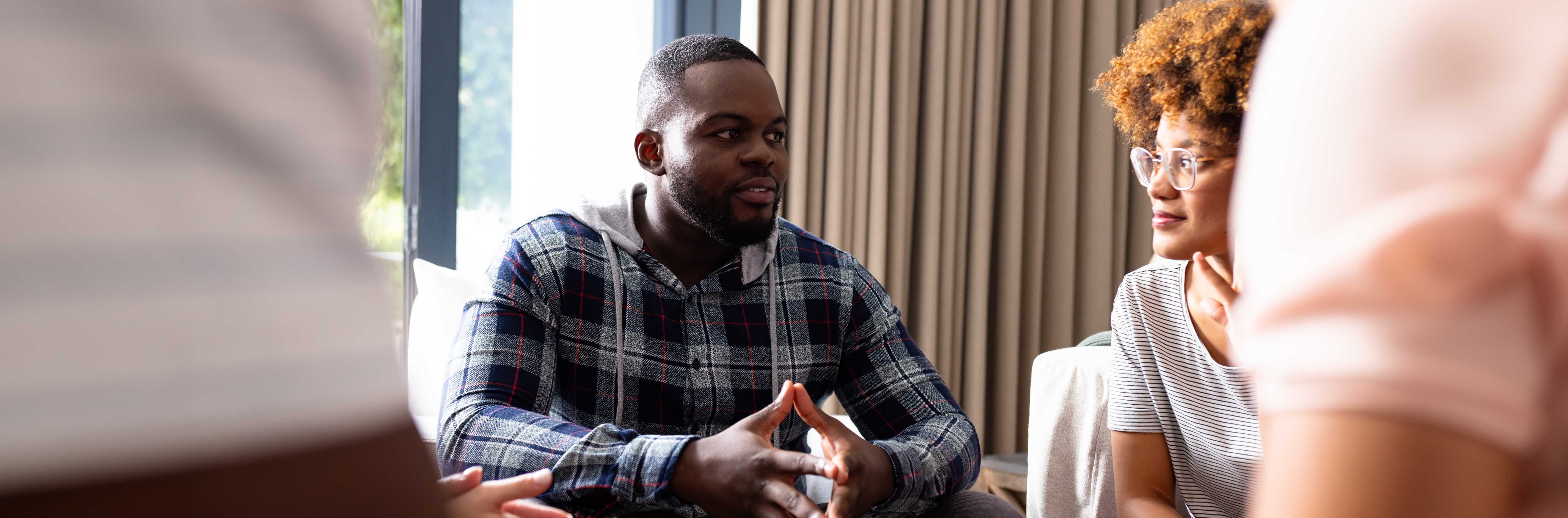 Young adults sitting in a circle in a group counselling session, listening compassionately to one another.