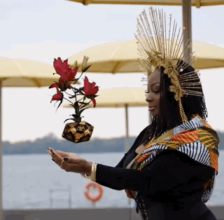 A Black woman in costume with an elaborate crown holding her hands out under a hovering CGI element.