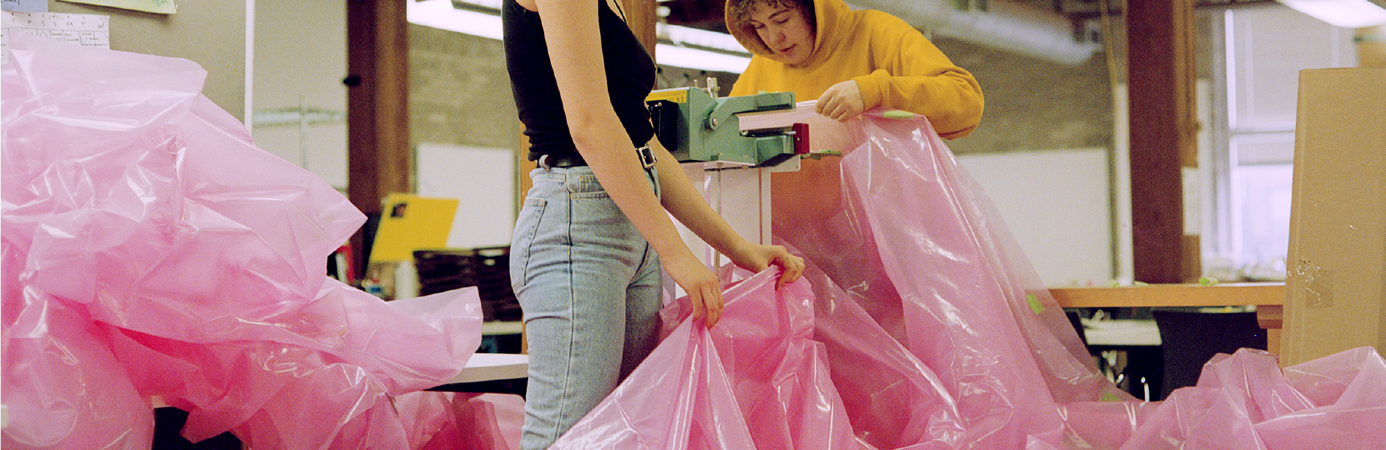 Emily Allan and Dominique Di Libero sealing sheets of pink plastic sheeting together.