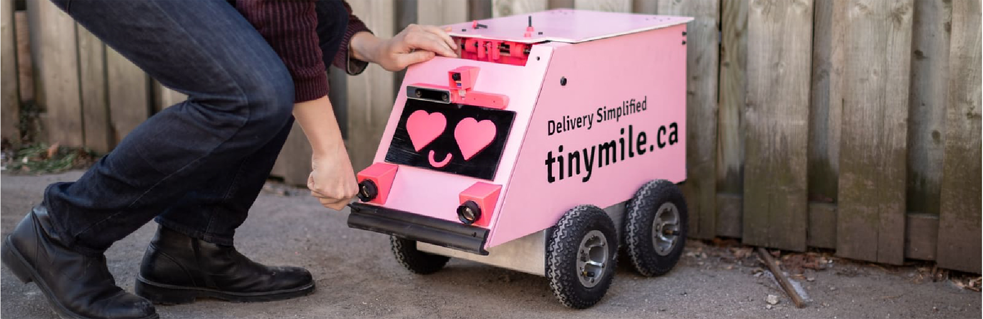 Person bending towards a pink wheeled robot with heart shape eyes.