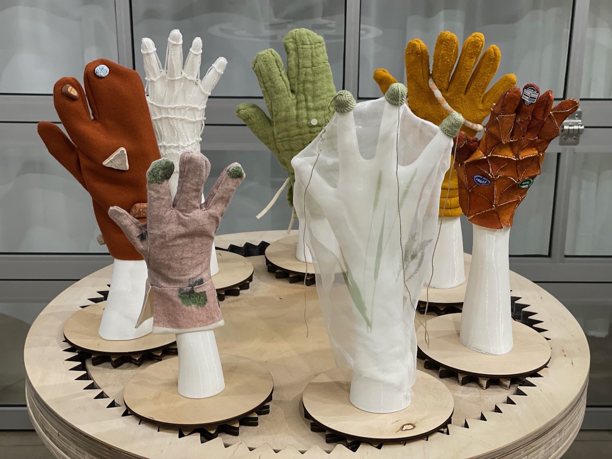 White 3D printed hands with various coloured gloves, arranged on a plywood gear base.