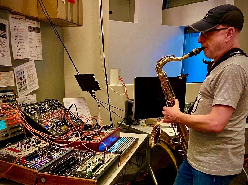 Jason Nolan playing the saxophone while looking at a control board.