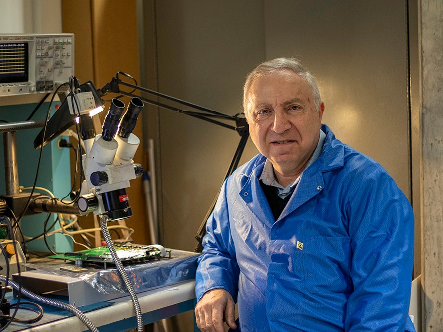 In his research lab, professor Lev Kirischian sits at a work desk with a microscope aimed at a circuit board.