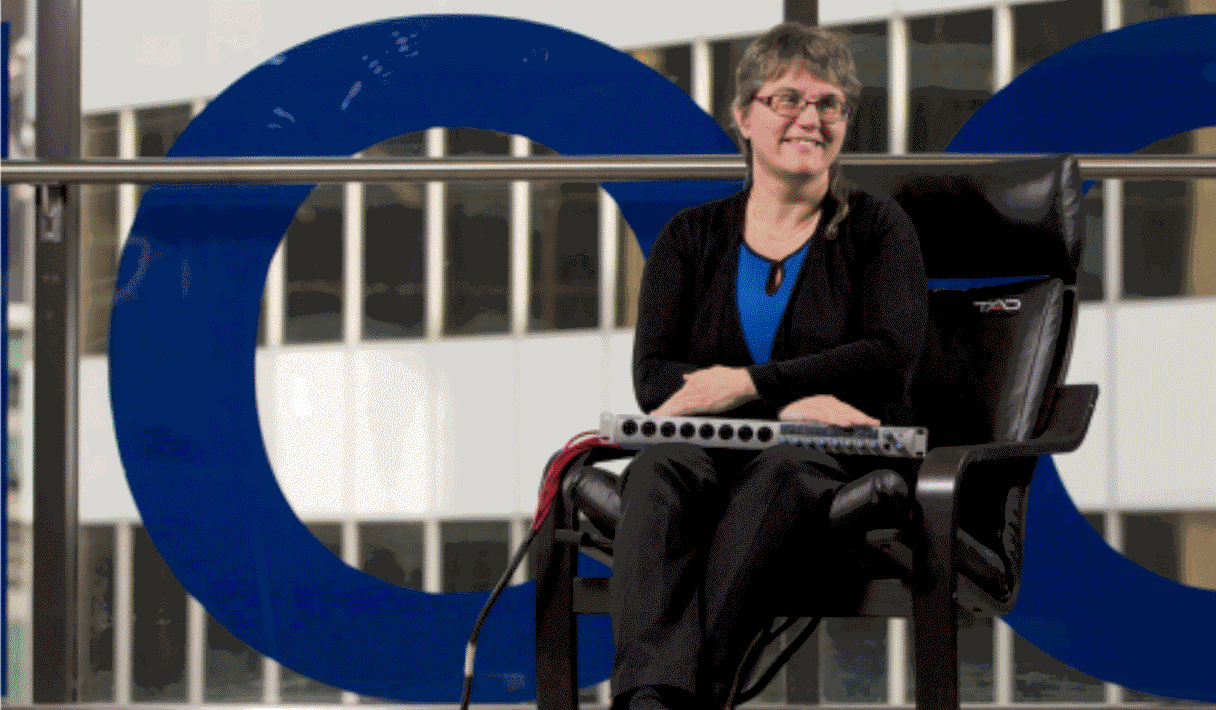 Dr. Deborah Fels smiling and sitting in the TAD chair in front of window at TRSM building with IMDC technology in her lap