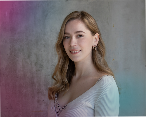 "A portrait of Emily Hall smiling against a light grey concrete wall. She has long, wavy blonde hair and is wearing a white cardigan. The image features a bright pink-to-purple colour overlay on the left side and a soft teal hue on the bottom right."