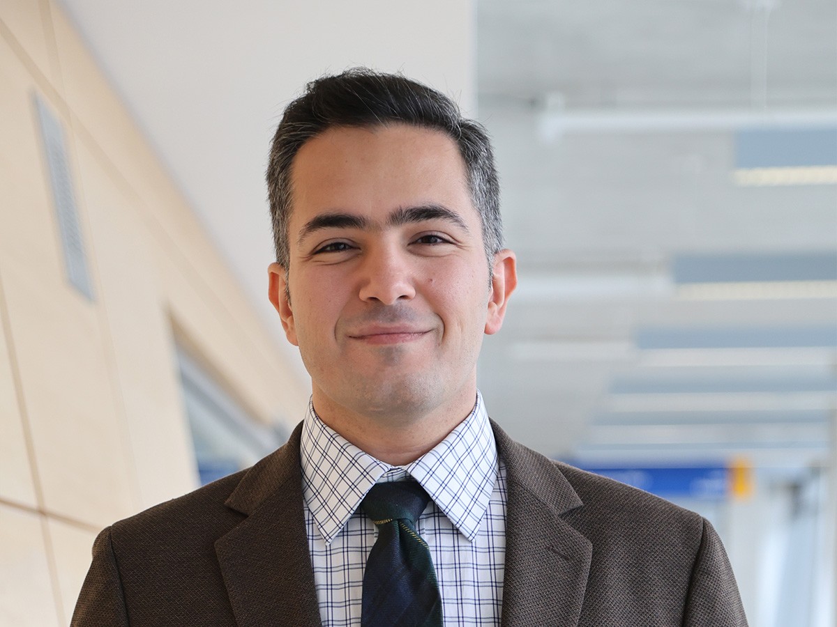 Dr. Mohammad Shushtari smiling standing in front of a garden and building.