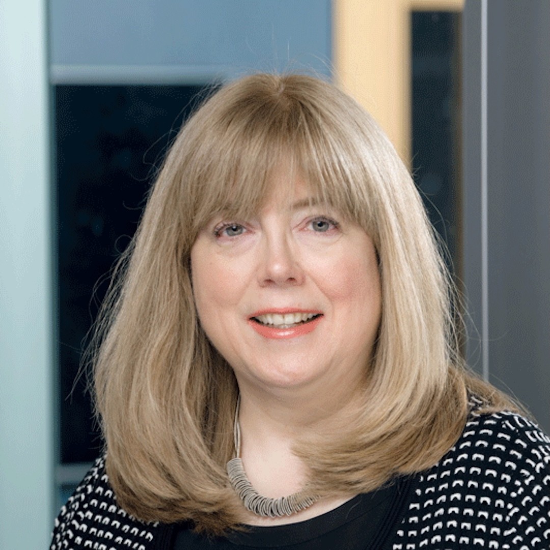 Close-up headshot of Carolyn Meyer. She is wearing a patterned black and white top, large textured necklace, and wearing her light blonde hair down with bangs,