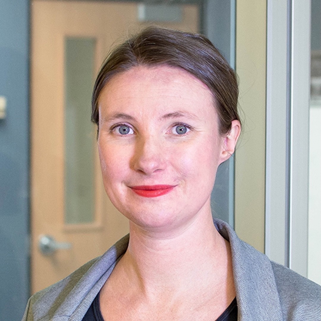 Close-up headshot of Jane Griffith. She is smiling slightly and wearing red lipstick. She is wearing a grey cardigan and has her light brown hair tied back.