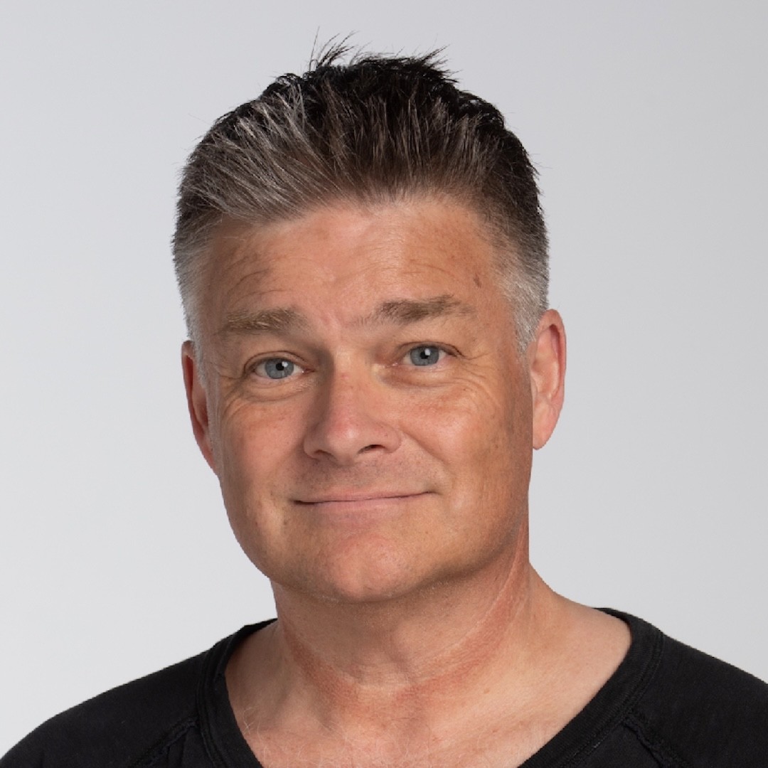 A close-up headshot of Robert Clapperton smiling. He has short dark grey hair, blue eyes, and is wearing a black shirt with a rounded neckline.