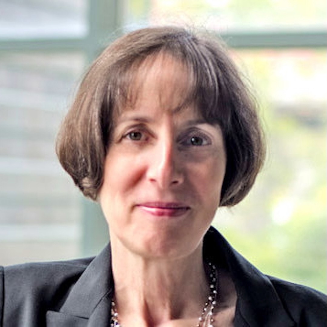 A close-up headshot of Wendy Freeman. She has a neutral expression and short light brown hair with bangs. She is wearing a dark grey blazer and layered necklaces.