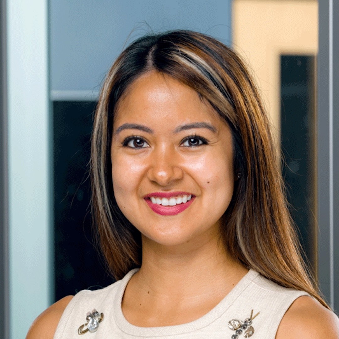 A close-up headshot of Dianne Nubla smiling. She has long brown hair and a beige sleeveless top.