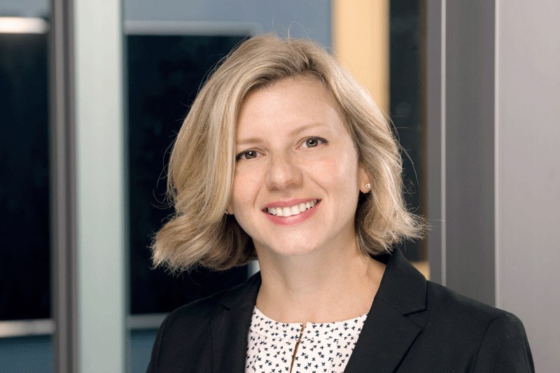 Dr. Eva Woyzbun smiles at the camera. She is wearing a black blazer and white and black patterned shirt. 