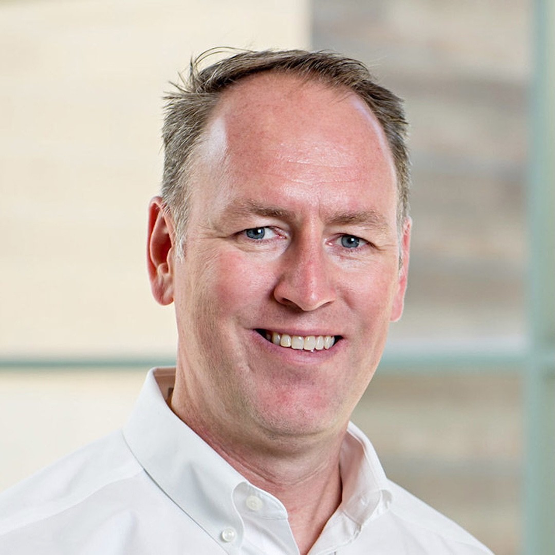 A close-up headshot of Richard McMaster smiling. He has short light brown hair and if wearing a white button-up shirt.