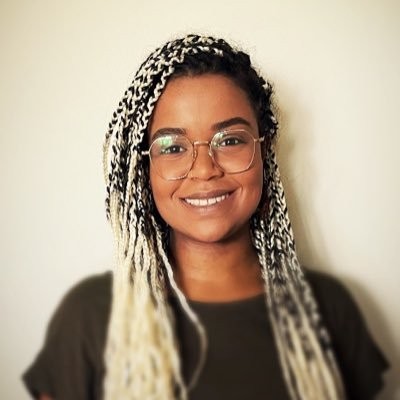 Smiling Black woman with gold-rimmed glasses and dyed blonde and black braided hair