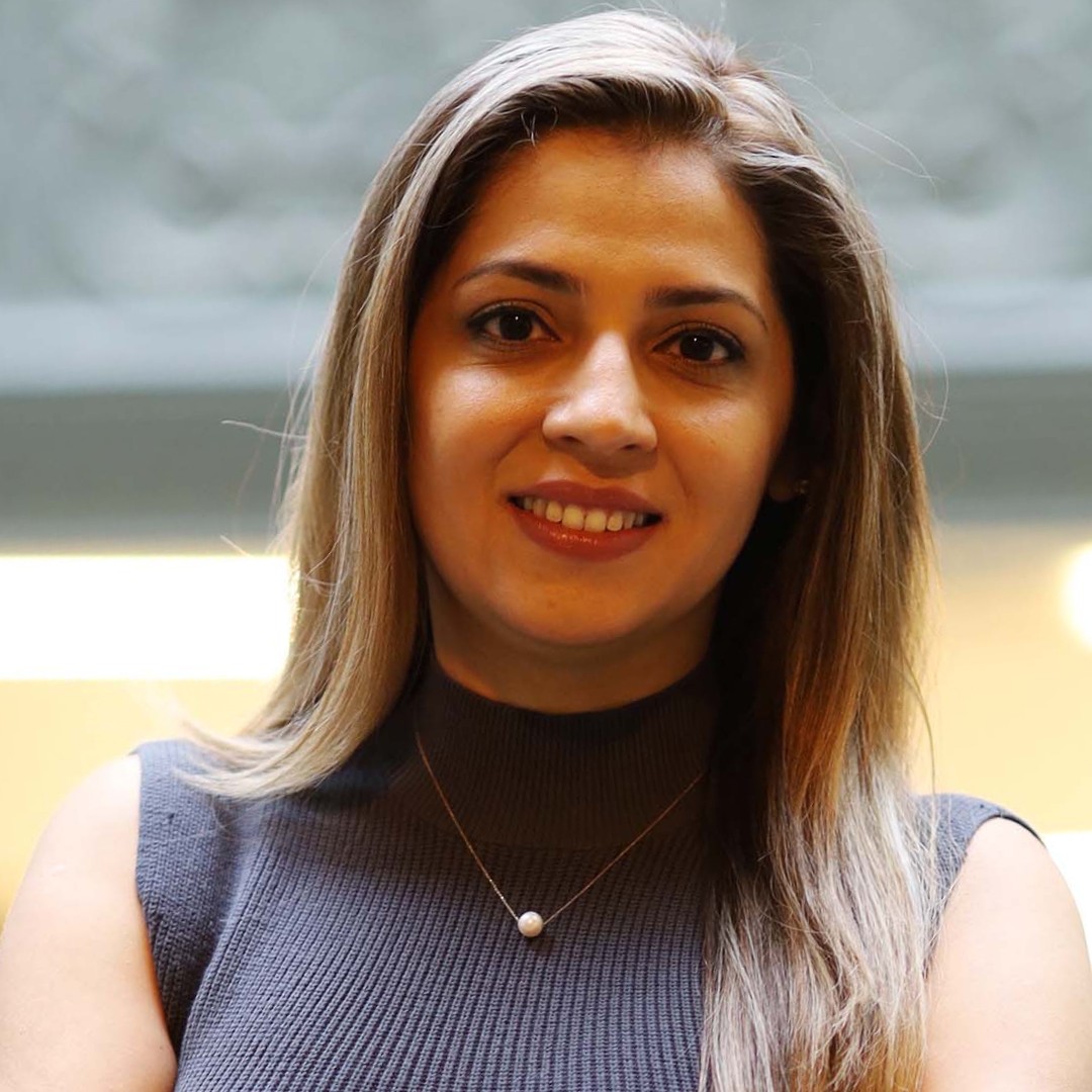 Close-up headshot of Afsoon Soudi smiling. She has straight hair parted to the side and is wearing a sleeveless dark grey top with a necklace.